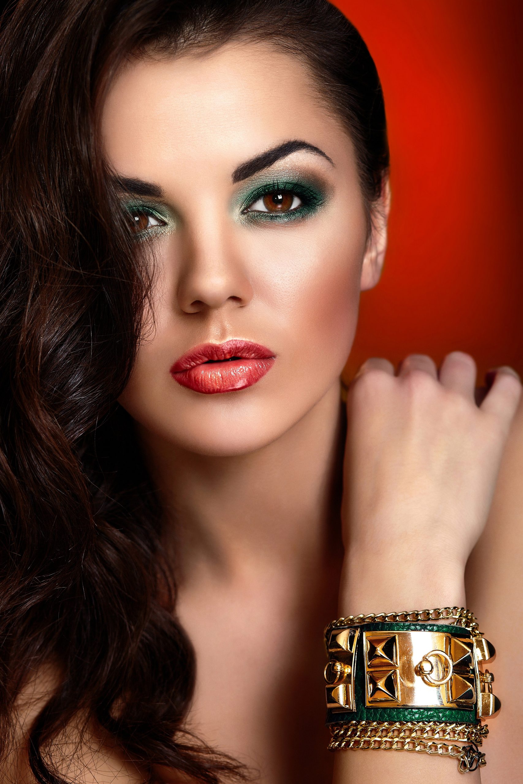 High fashion look.glamor closeup portrait of beautiful sexy Caucasian young woman model with red lips,bright green makeup, with perfect clean skin with jewelery on hand isolated on red background